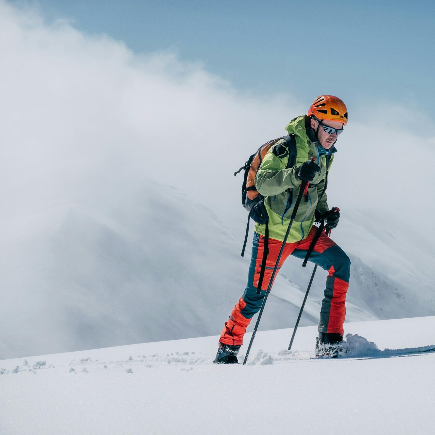 A skier trekking uphill on a snowy mountain in bright winter gear, under a clear sky.