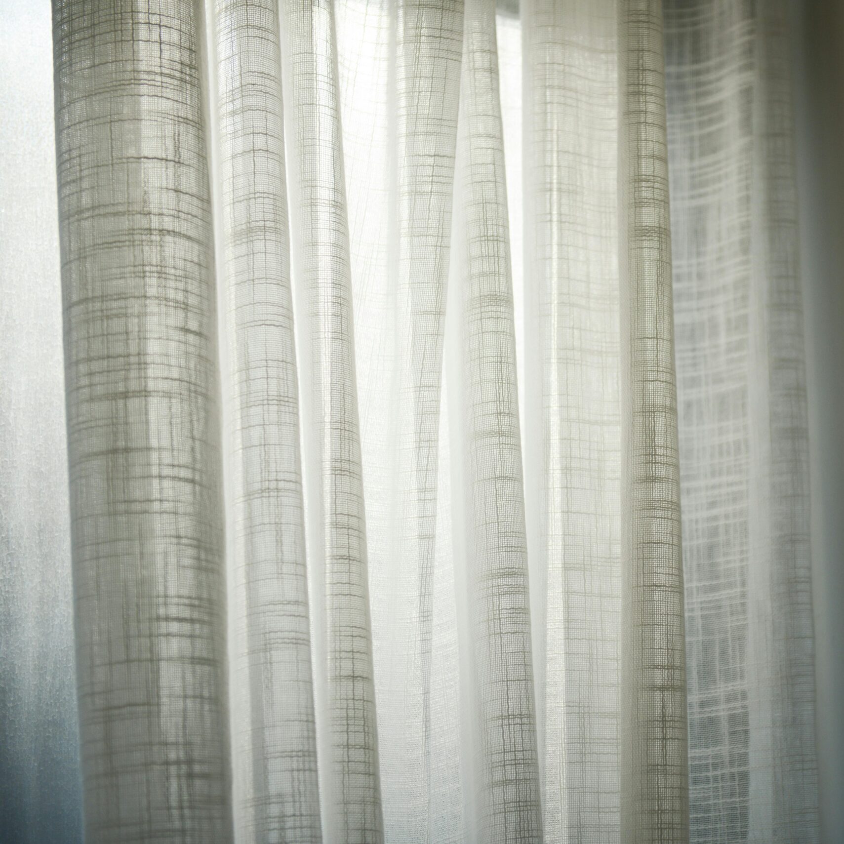 Sheer white curtains gently lit by daylight create subtle shadows on the wall.